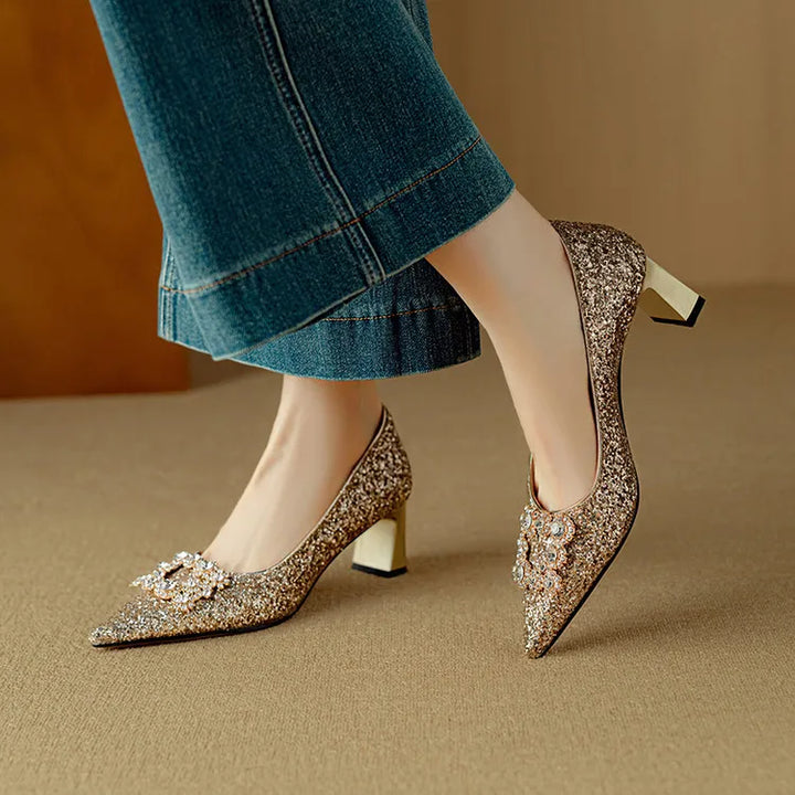 Woman wearing glitter block heel pumps with a pointed toe on a plain background.