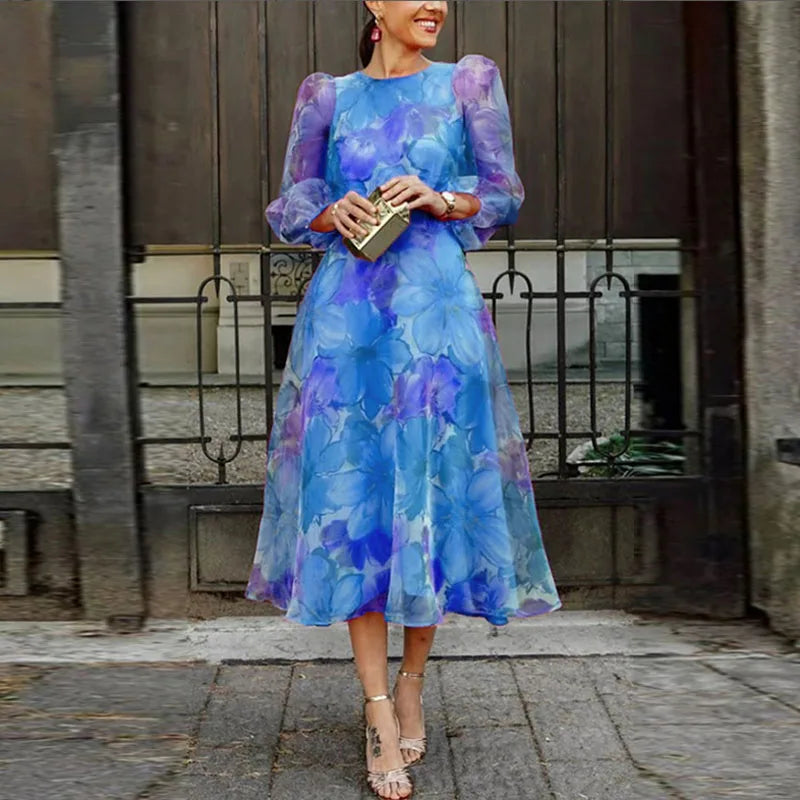 Woman posing in a floral A-line midi dress with puff sleeves on a plain background.