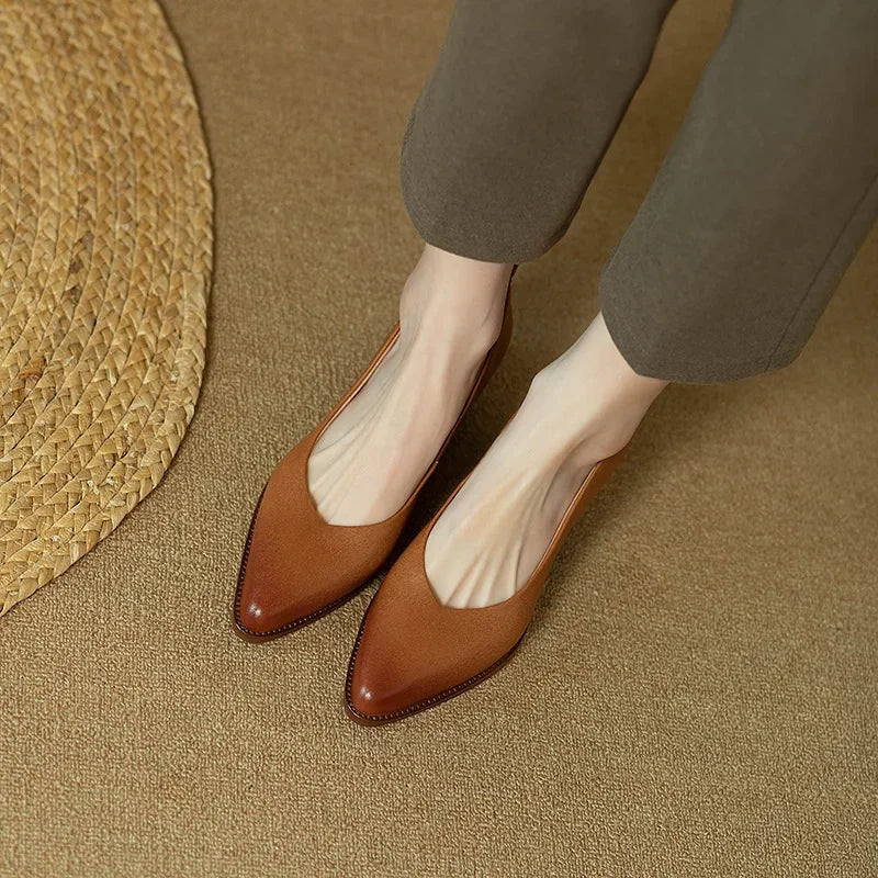 Woman wearing polished pointed pumps with a steady heel on a plain background.