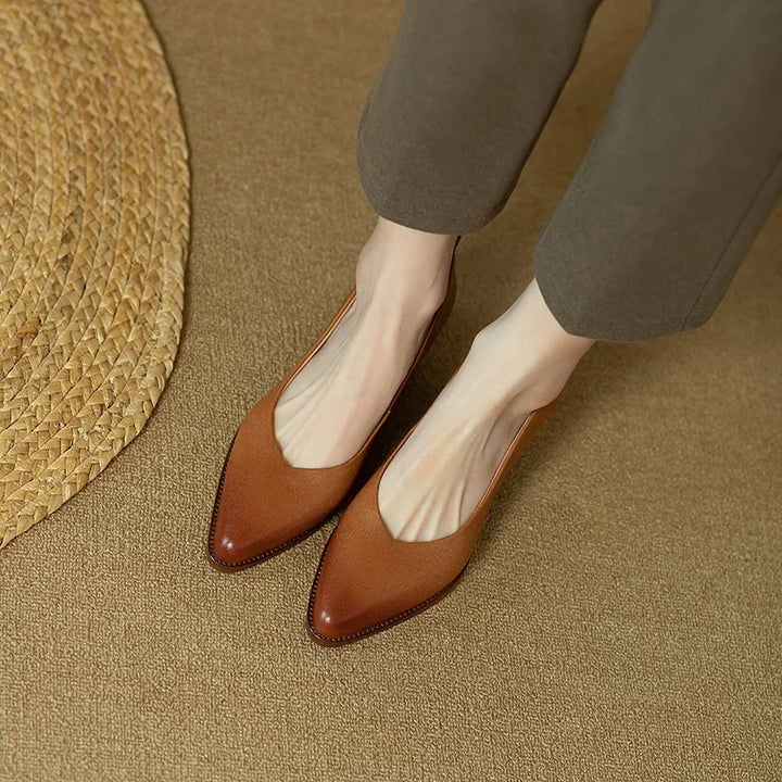 Woman wearing polished pointed pumps with a steady heel on a plain background.