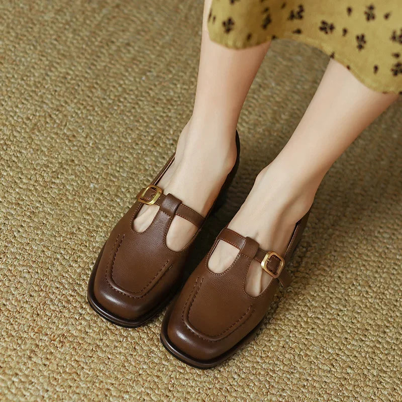 Woman wearing square toe strap shoes with a low block heel on a plain background.
