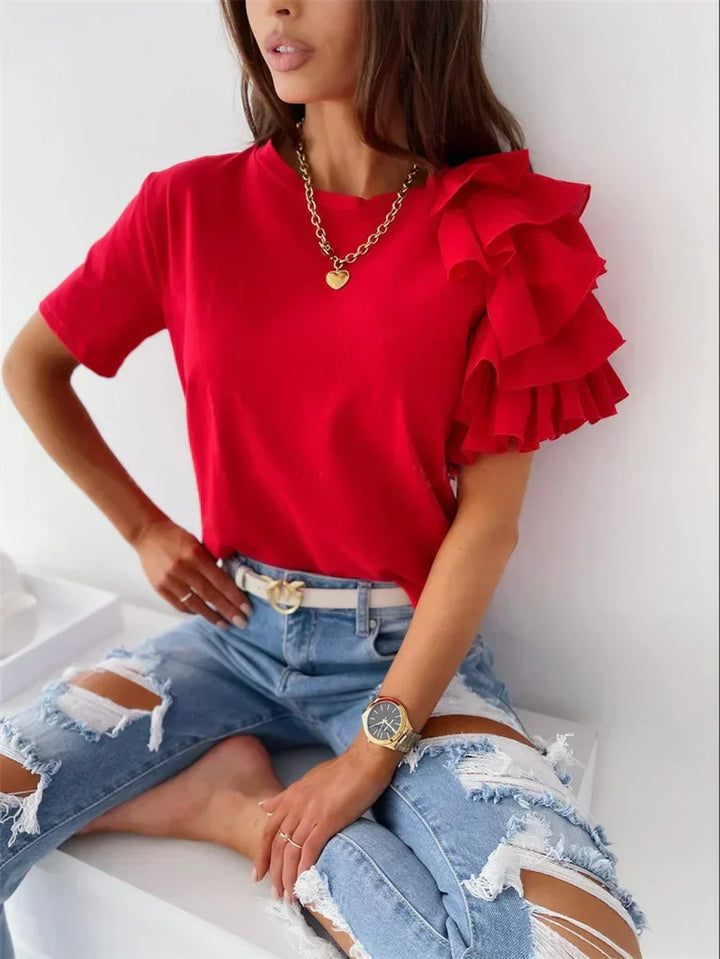 Woman wearing a flowing blouse with ruffle sleeves against a plain background.