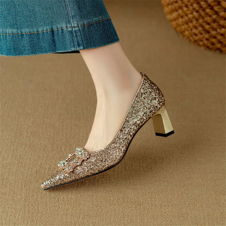 Woman standing in glitter pointed toe heels with a sturdy block heel on a plain background.