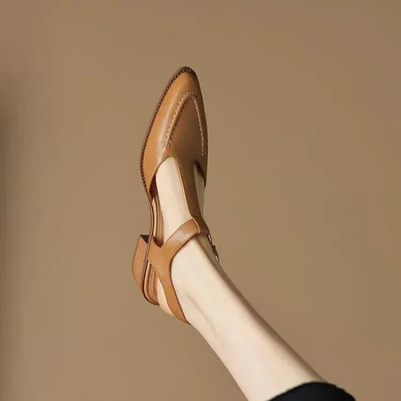 Female model standing in tan buckle strap shoes on a plain background.