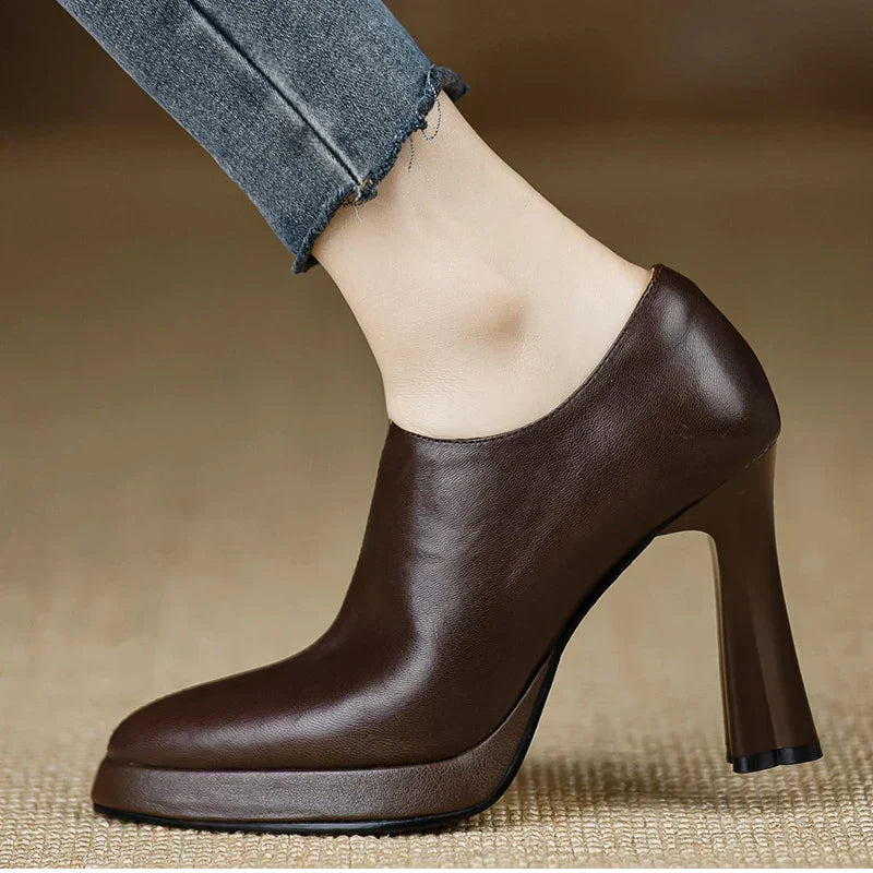 Female model wearing dark brown platform heel pumps with a side zip on a plain background.