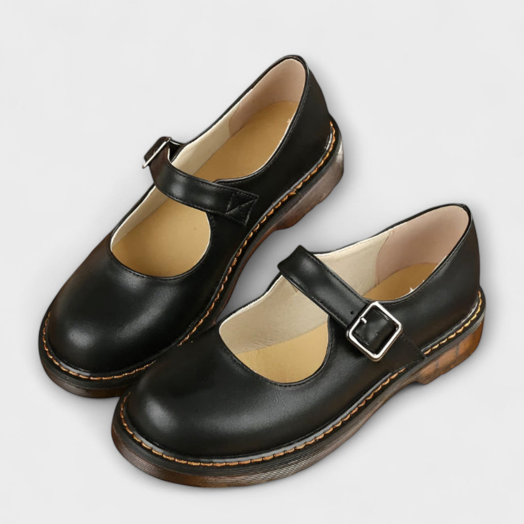 Woman showcasing rounded toe Mary Jane flats on a plain background.