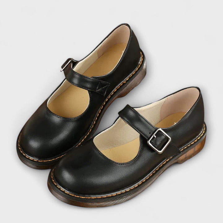 Woman showcasing rounded toe Mary Jane flats on a plain background.