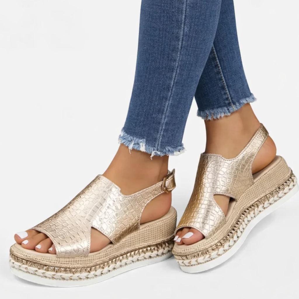 Female model showing metallic open-toe wedge sandals with a secure buckle strap on a plain background.