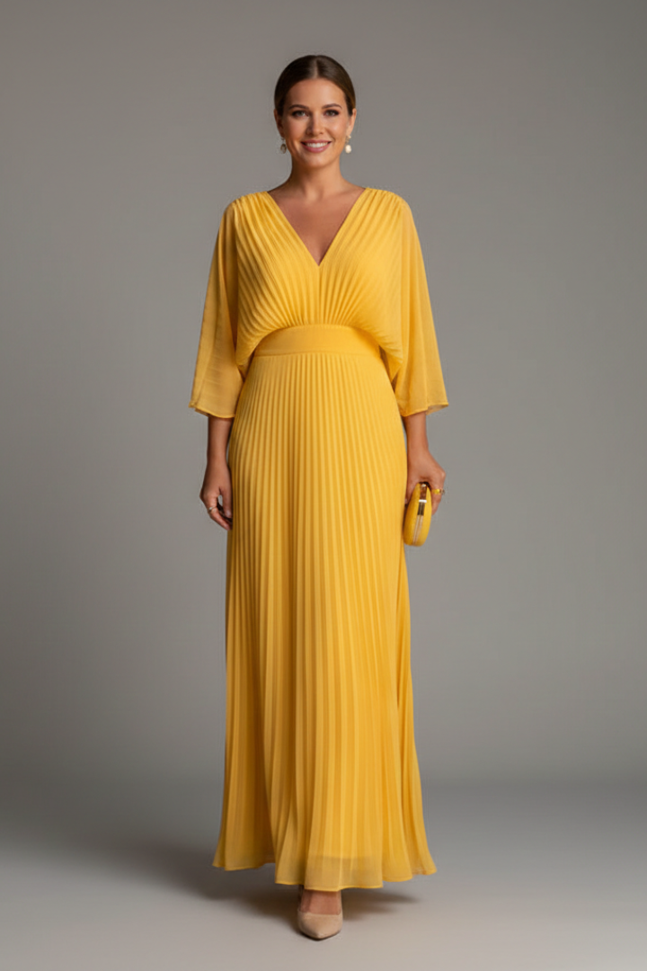 Woman wearing a long dress with a smooth upper section and pleated lower section on a plain background