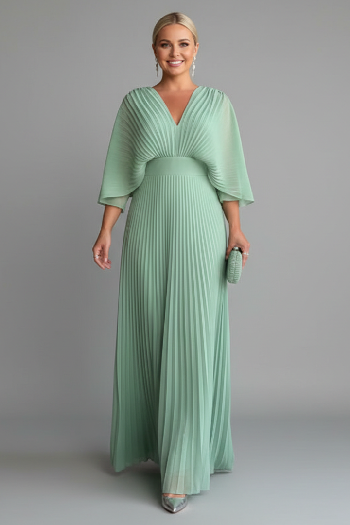 Woman wearing a flowing pleated dress with long sleeves and a V-neckline on a plain background.
