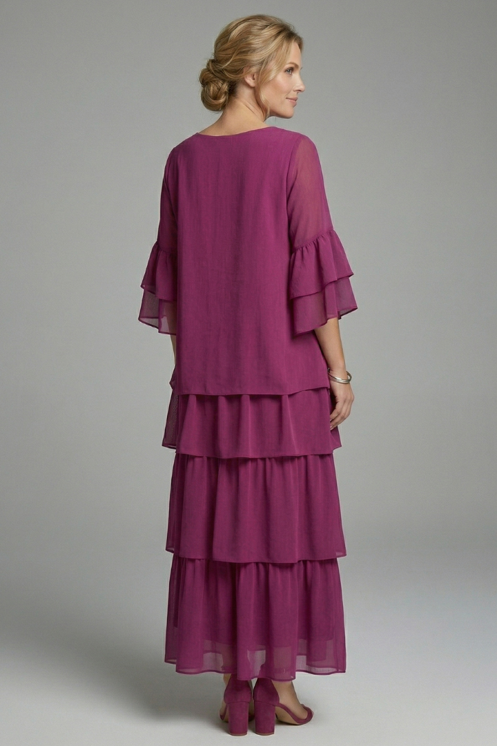 Woman in a loose short sleeve maxi dress with tiered skirt on a plain background.