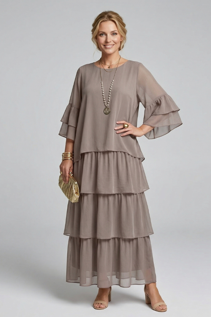 Woman wearing a plain woven look maxi dress with layered skirt on a plain background.