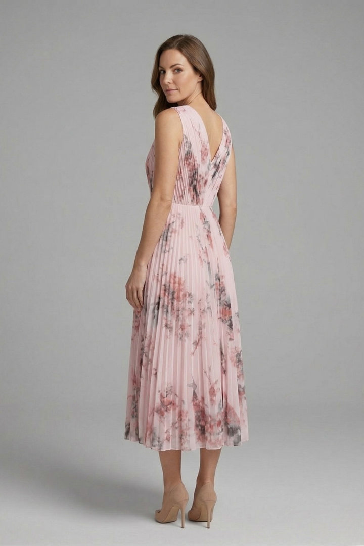 Woman wearing a V-neck dress with a pleated midi-length skirt against a plain background.