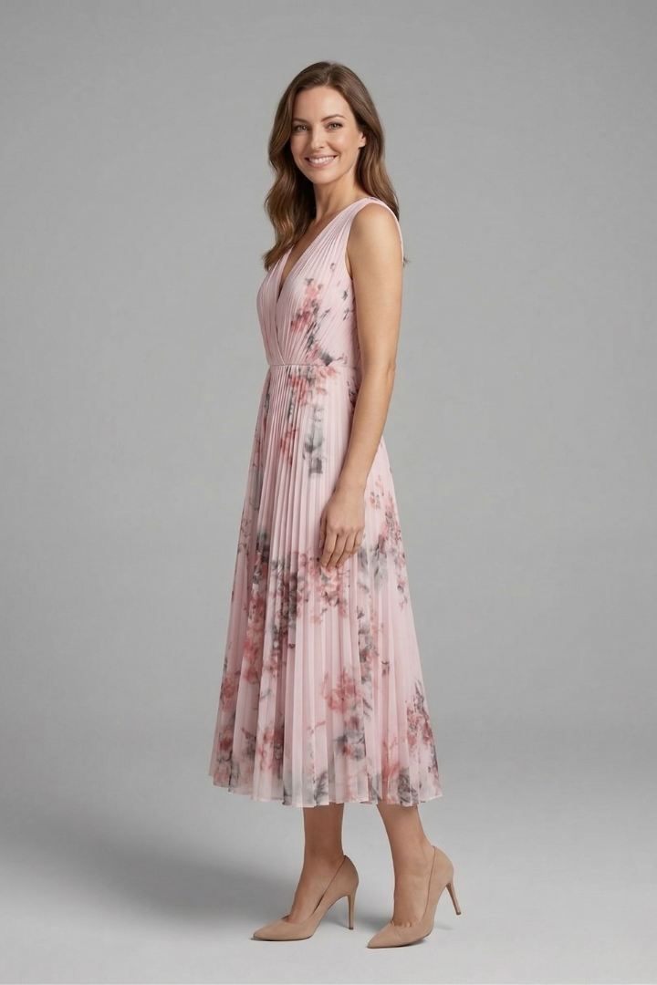 Woman in a printed sleeveless dress featuring a V-neckline and flowing pleated skirt on a plain background.
