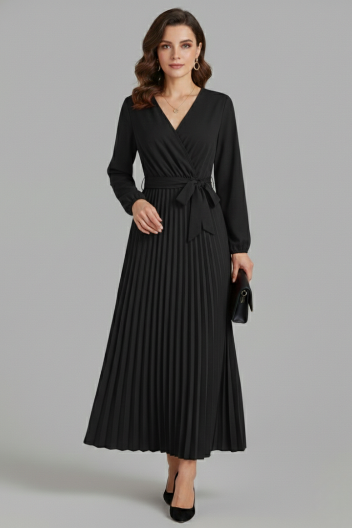 Woman in a pleated maxi dress with a waist tie and V-neckline on a plain backdrop.