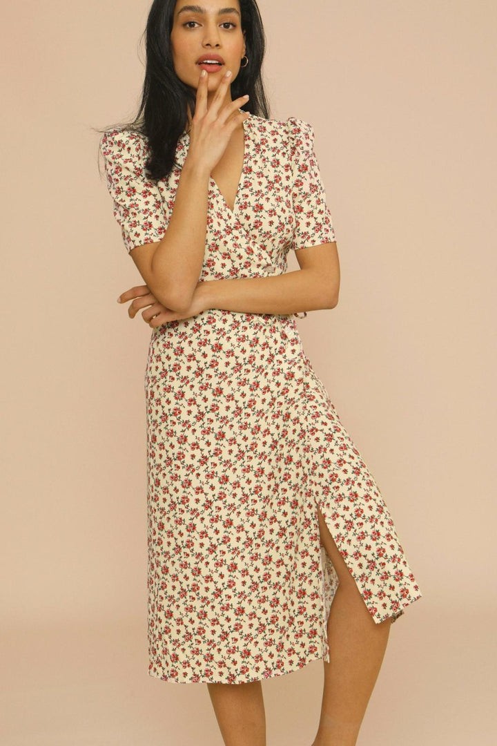 Woman posing in a flowing floral midi dress with soft daytime styling on a plain background.