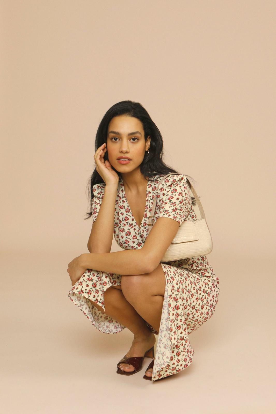 Woman in a floral midi dress styled for spring and summer occasions on a plain background.