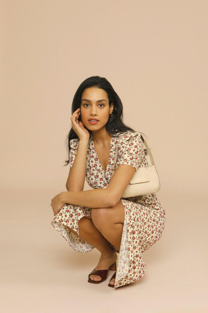 Woman in a floral midi dress styled for spring and summer occasions on a plain background.