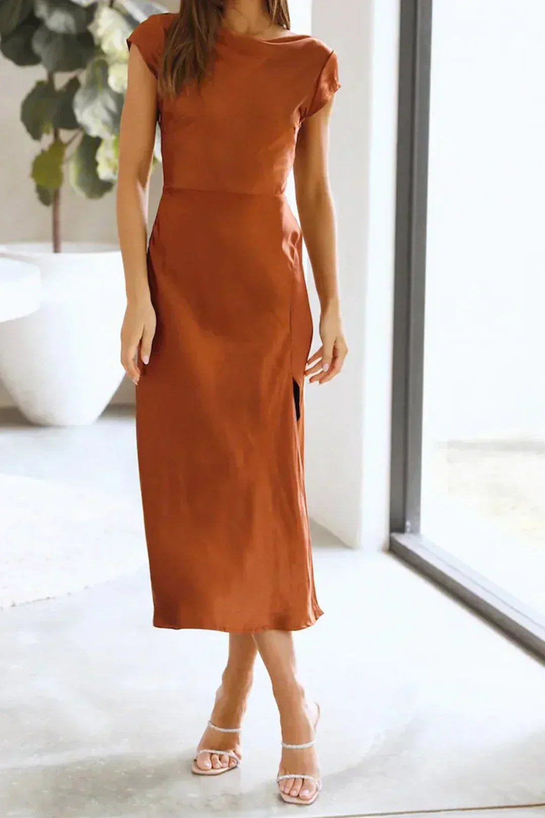 Woman posing in a sleek midi slip dress with a clean silhouette on a plain background.