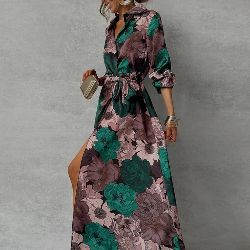 Woman posing in a botanical print maxi dress with waist tie and button-front design on a plain background.