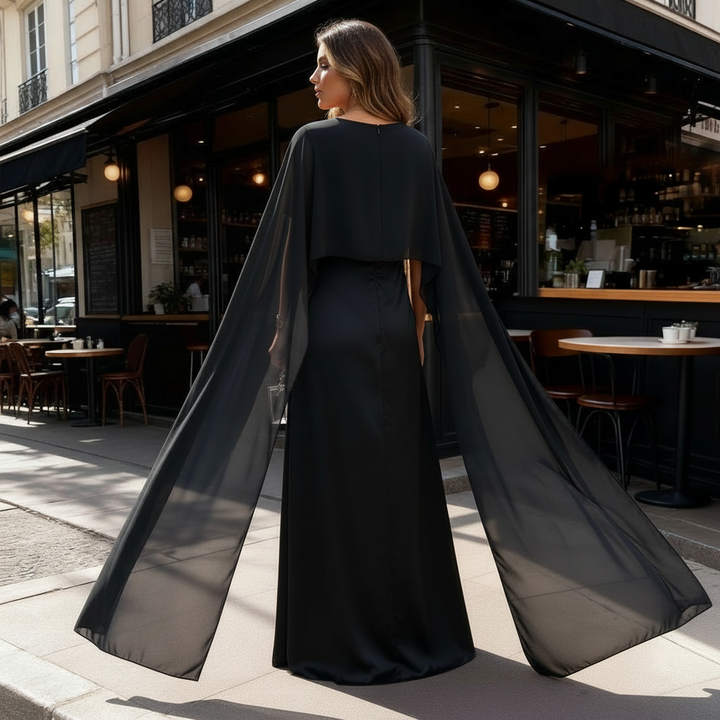 Female model in a flowing cape maxi dress on a plain background.