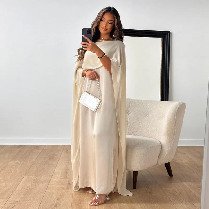 Female model wearing a formal cape maxi dress on a plain background.
