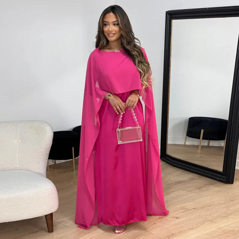 Woman wearing a long occasion dress with cape sleeves on a plain background
