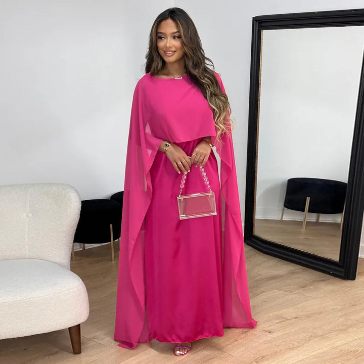 Woman wearing a long occasion dress with cape sleeves on a plain background