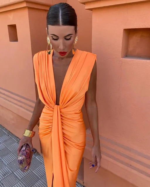 Model in a deep neckline ruched dress with front split on a plain background.
