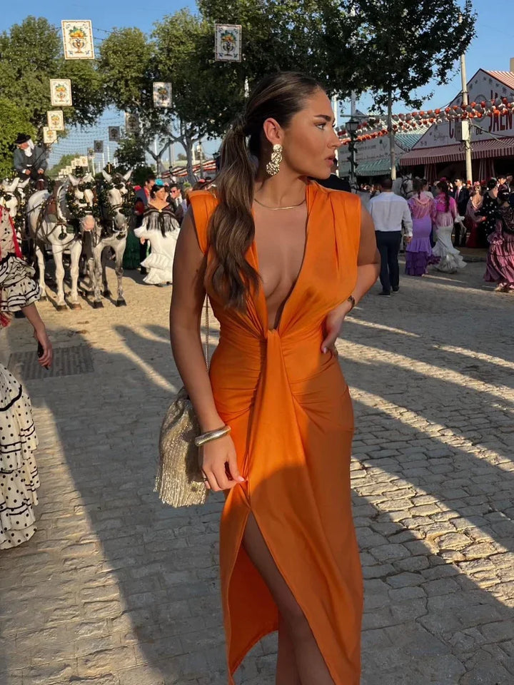Woman in a deep V ruched maxi dress with front split on a plain background.