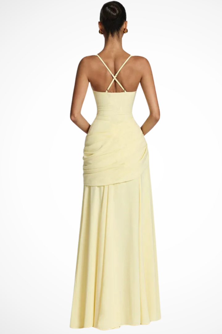 Woman in a floor-length formal dress with draped skirt detail against a plain background.