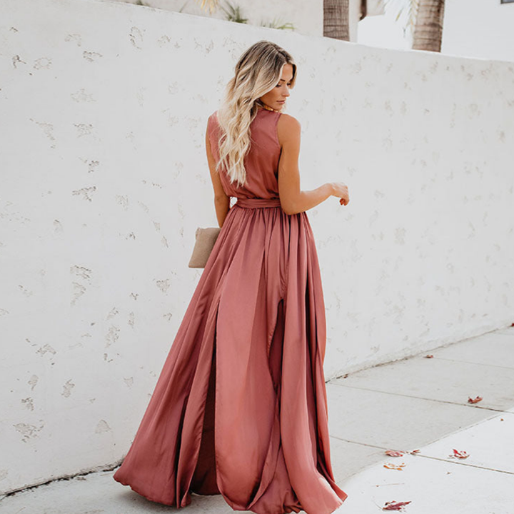 Woman posing in a flowing sleeveless maxi dress with waist tie on a plain background.
