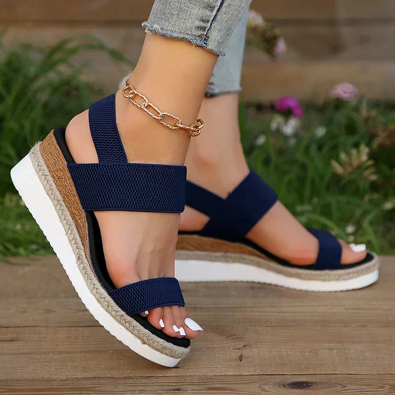 Female model wearing easy walking sandals on a plain background with a simple outfit.