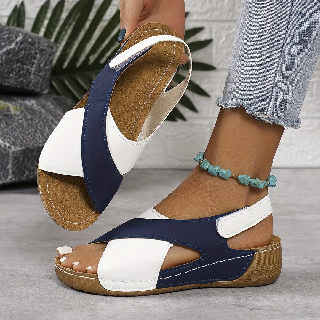Woman standing in strappy walking sandals on a plain background.