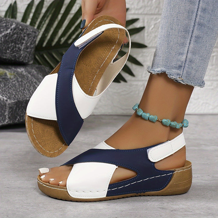 Woman standing in strappy walking sandals on a plain background.