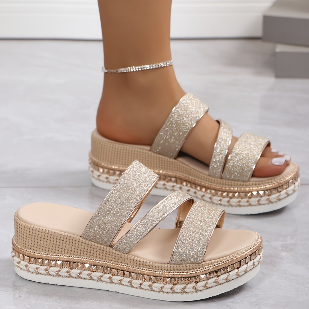 Female modelling lightweight sandals with shimmering straps on a plain background.