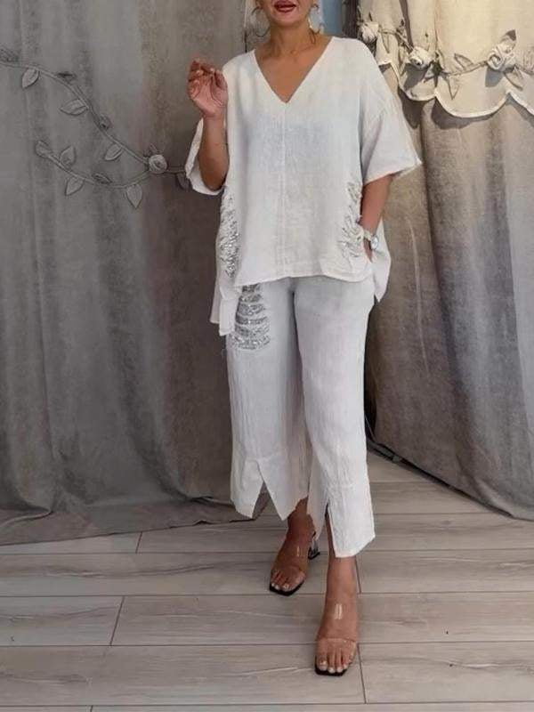 Woman showcasing a coordinated summer set featuring a relaxed top and flowing trousers on a plain background.