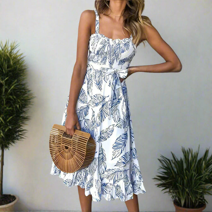 Female model in a sleeveless ruffle hem midi dress with nature-inspired print on a plain background.