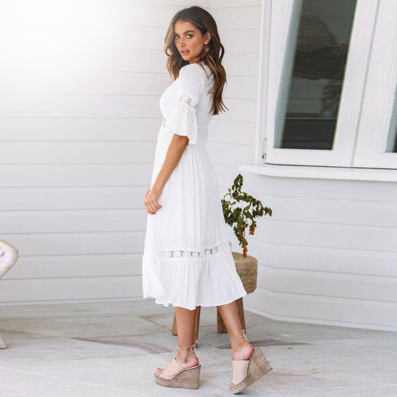Woman posing in a white tiered midi dress with lace trim on a plain background.