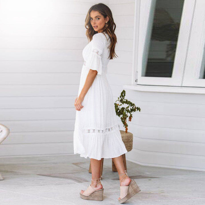 Woman posing in a white tiered midi dress with lace trim on a plain background.