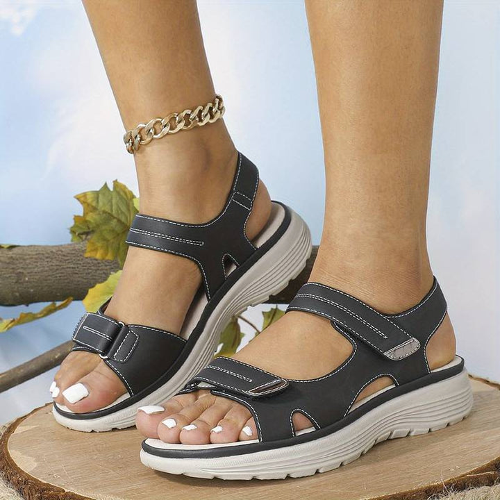 Female model wearing open toe walking sandals on a plain background.