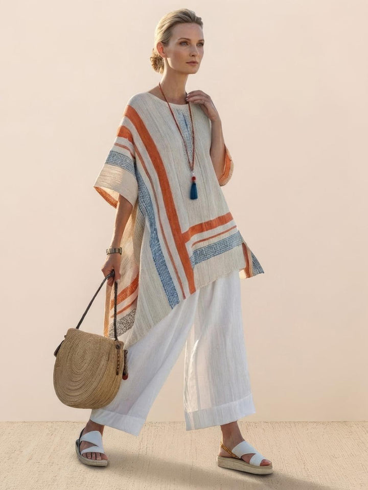 Woman wearing an embroidered tunic top paired with wide-leg trousers on a plain background.