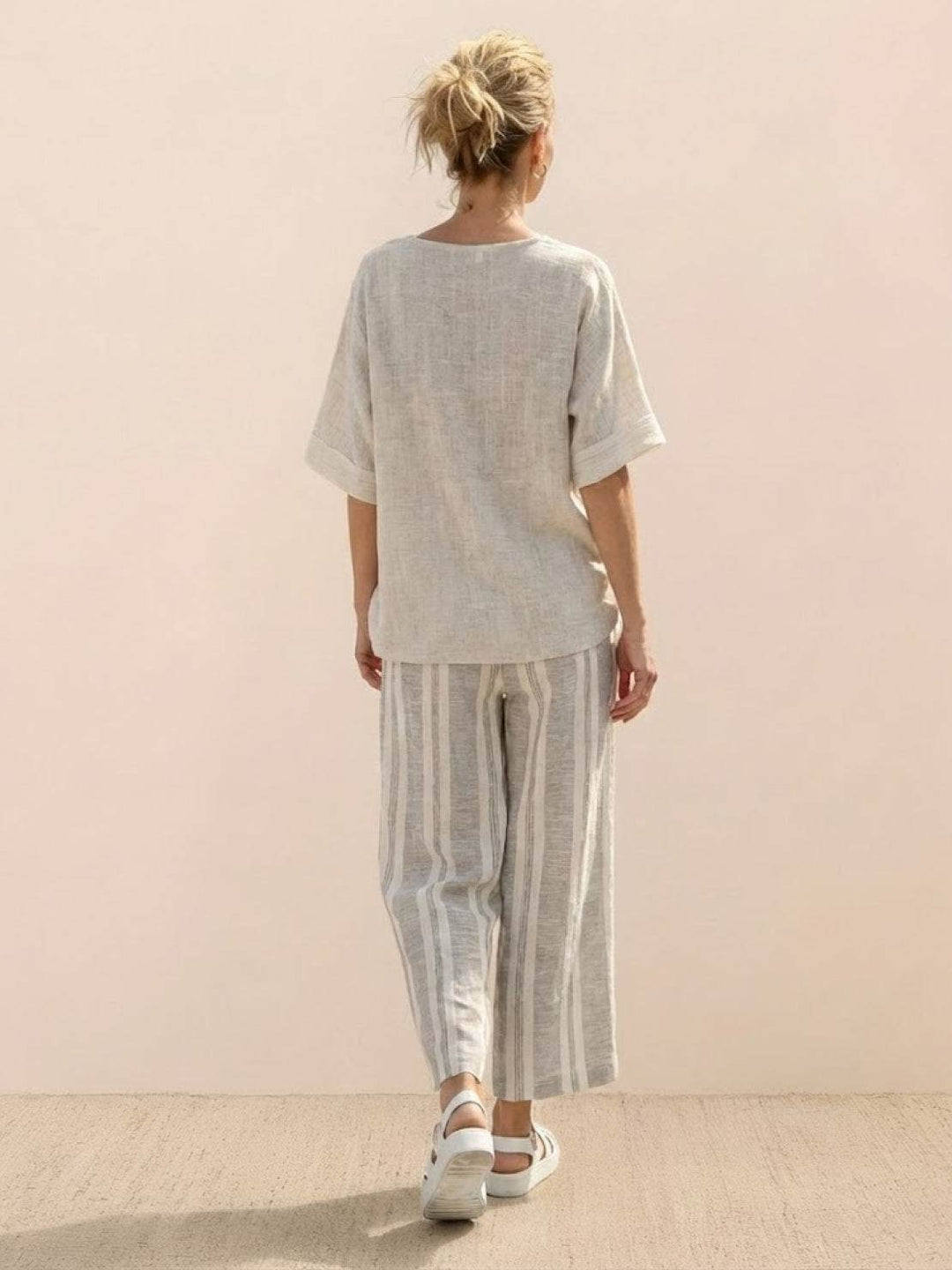 Woman in a striped two-piece set featuring embroidered trim and flowing wide-leg trousers on a plain background.