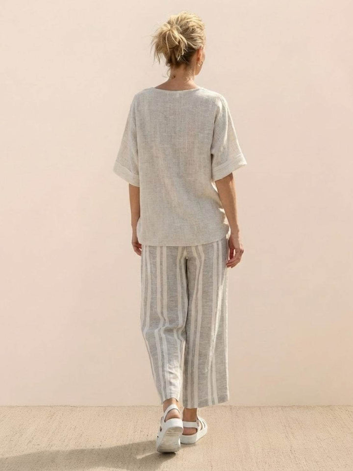 Woman in a striped two-piece set featuring embroidered trim and flowing wide-leg trousers on a plain background.