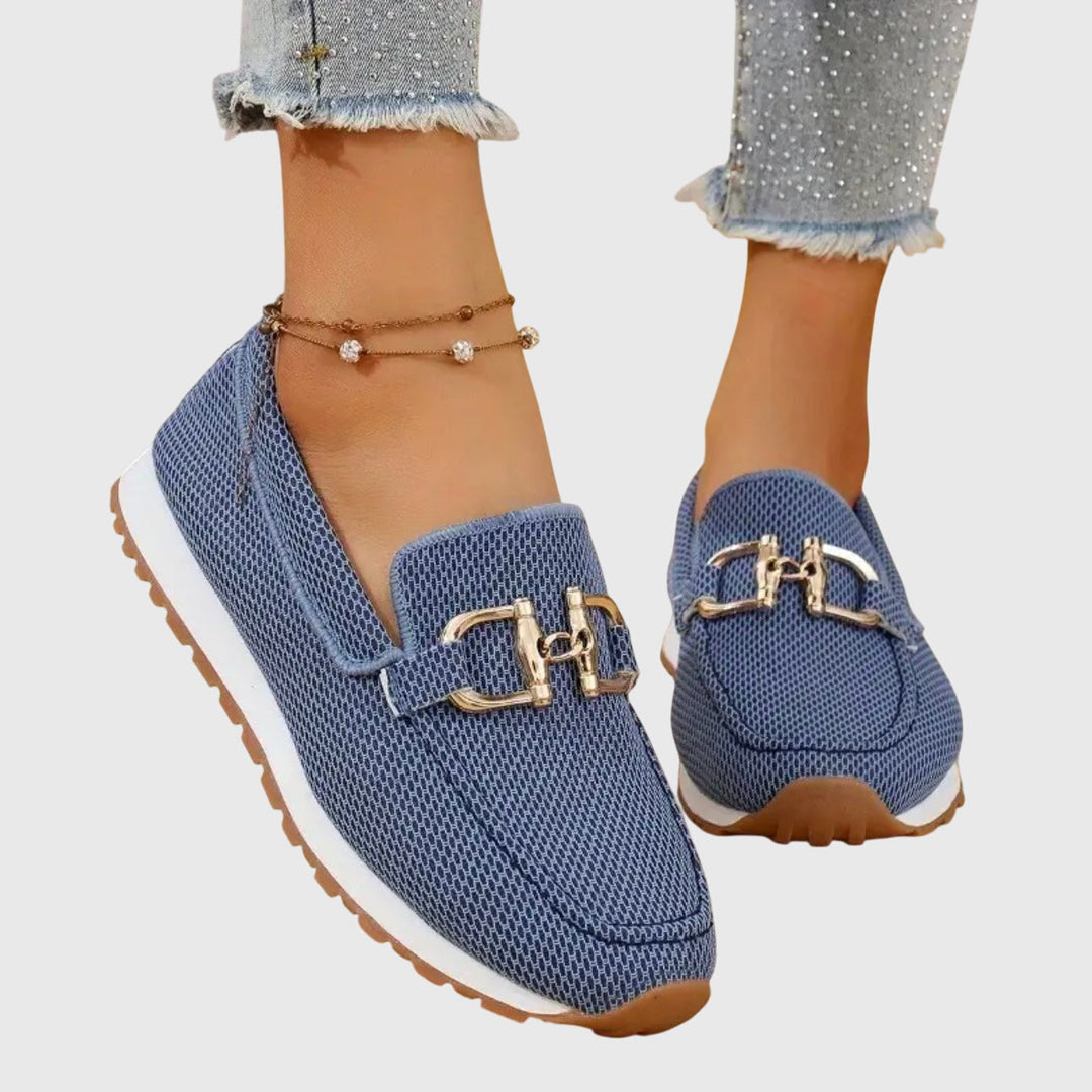 Woman standing in polished loafers against a plain background.