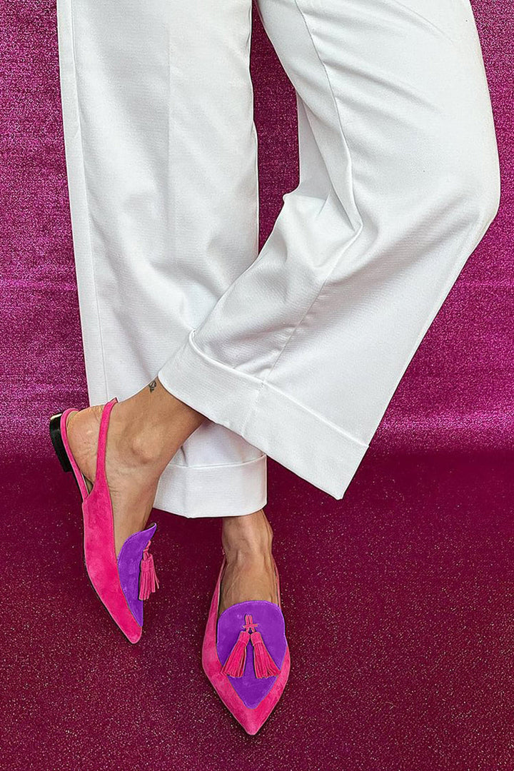 Women’s flat shoes with decorative ankle strap and fringe on a plain background.