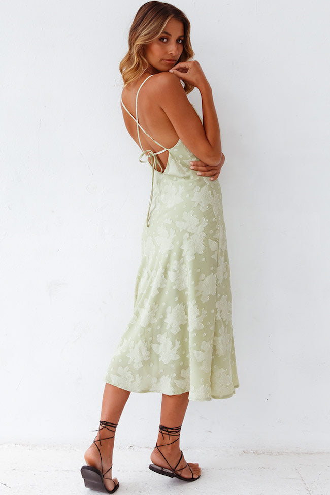  Woman in a floral midi dress featuring a flowing silhouette on a plain background.