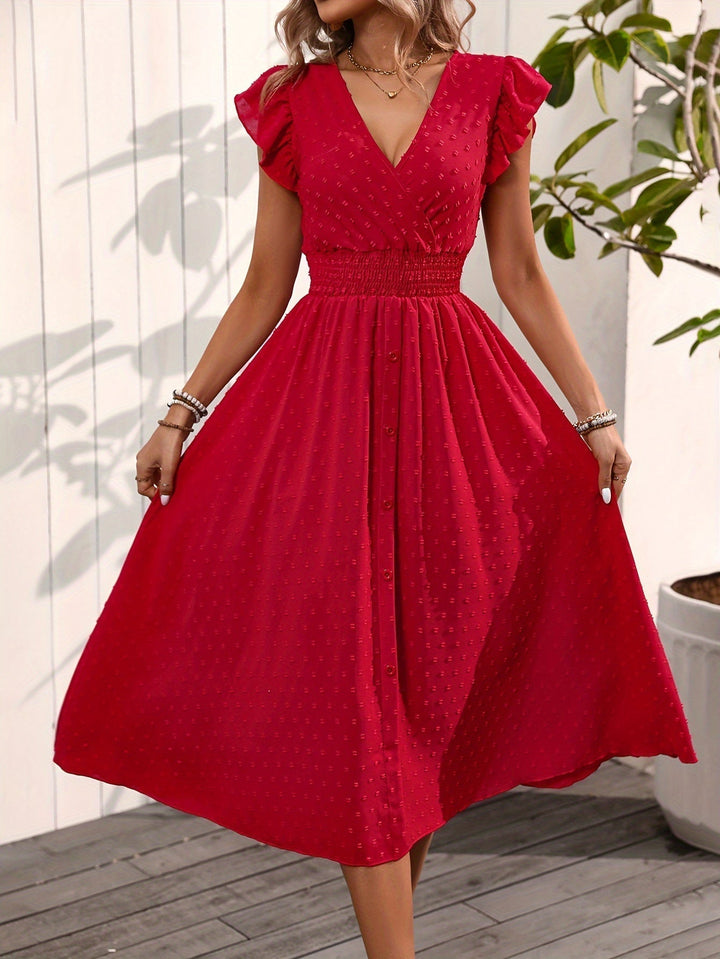  Female wearing a polka dot dress with soft shoulder ruffle details on a plain background.