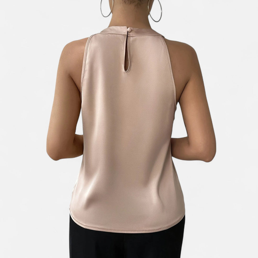 Model in a draped sleeveless top with a graceful neckline on a plain background.