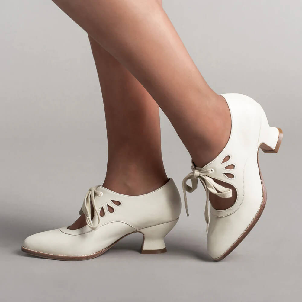 Female model standing in retro ankle strap heels on a plain background.